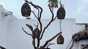 Una escultura de árbol con nidos colgando de sus ramas, sobre un fondo de pared blanca.