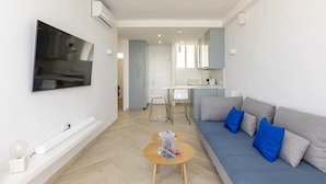 Una sala de estar moderna con un sofá gris, un televisor montado en la pared y una pequeña mesa de madera con un juego de mesa.