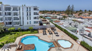 Un hotel moderno con zona de piscina en la azotea, que incluye tumbonas y un pequeño jacuzzi.