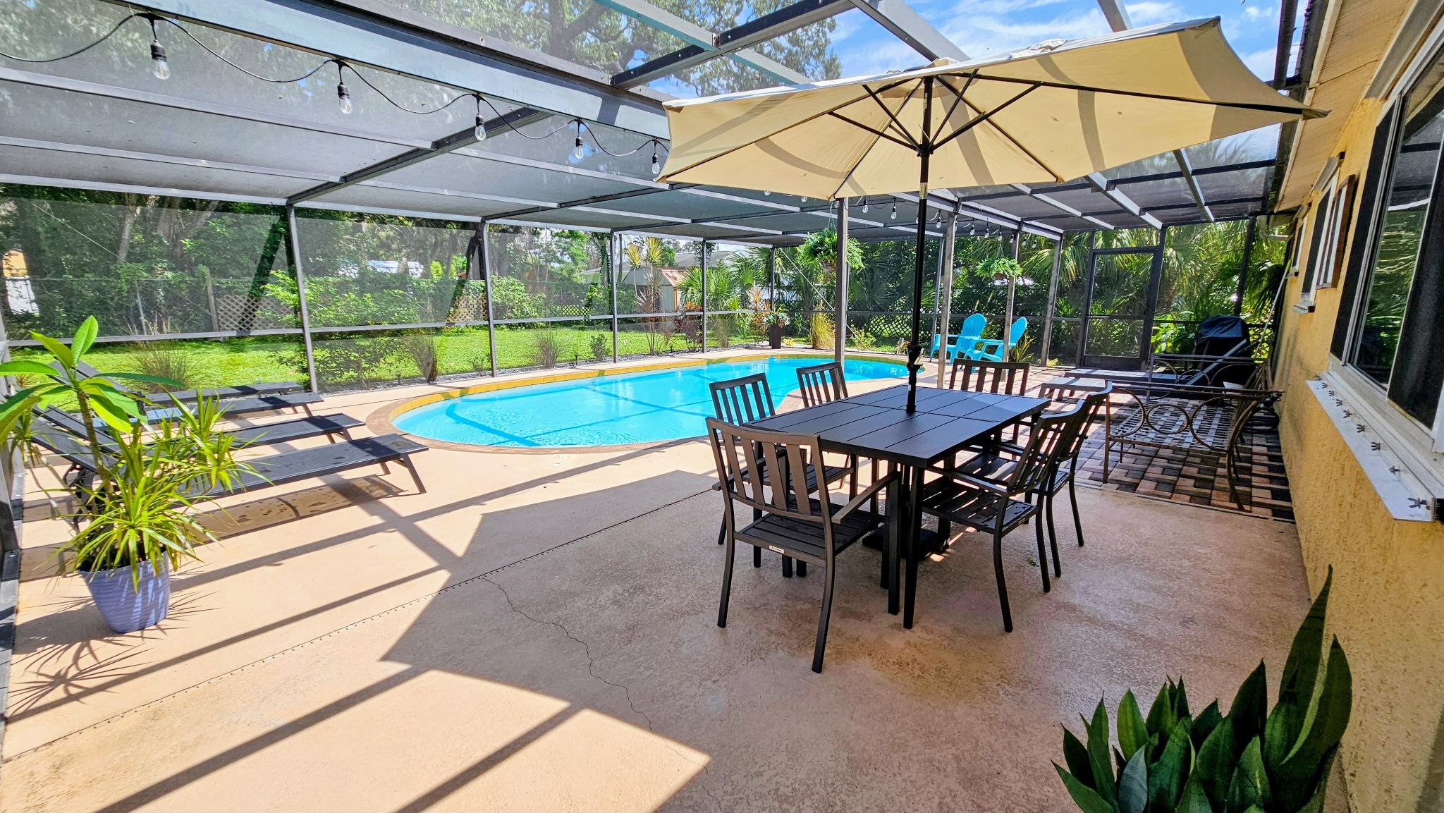 A covered outdoor area with a pool, a table, chairs, and potted plants.