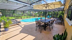 A covered outdoor area with a pool, a table, chairs, and potted plants.
