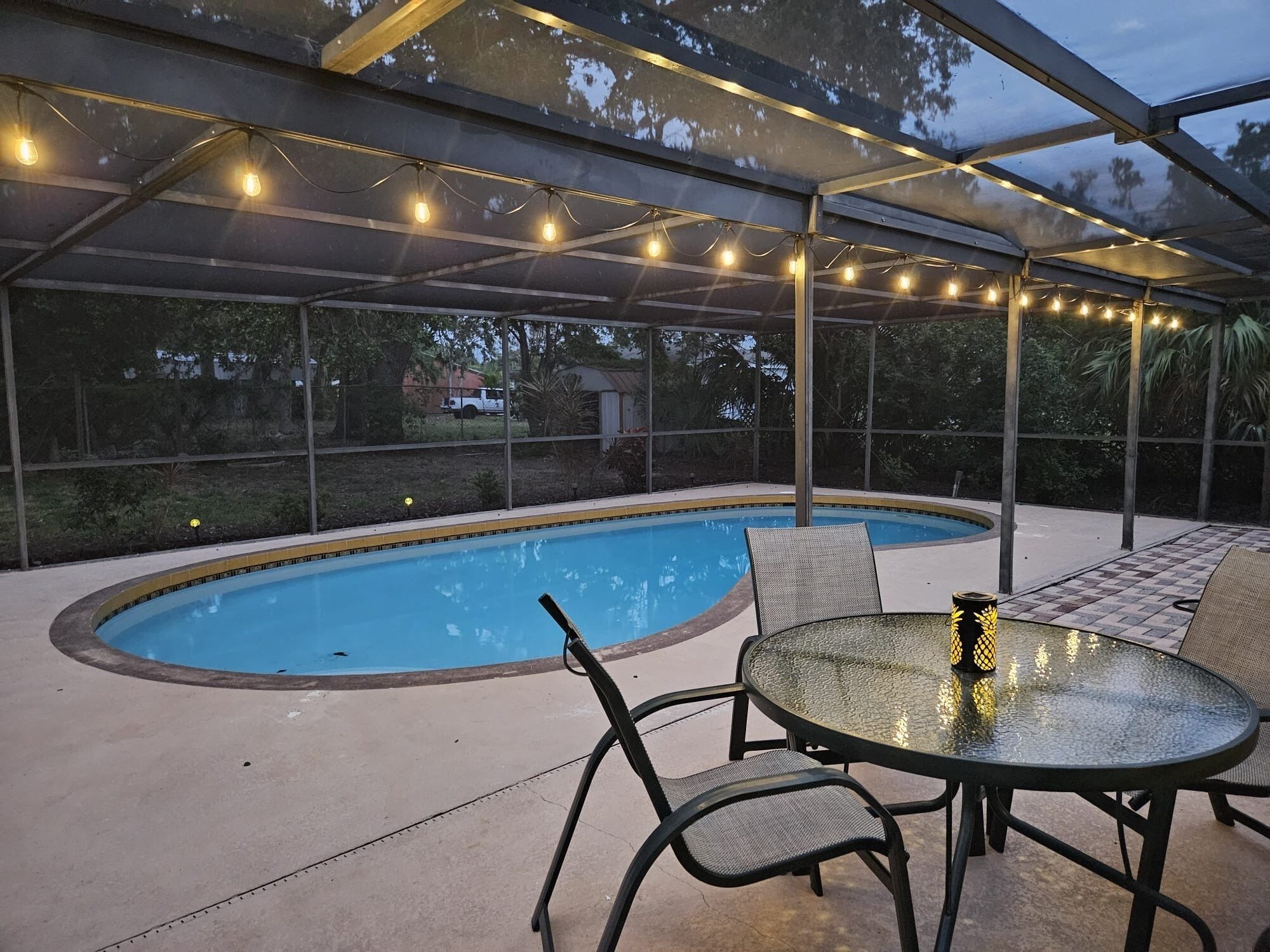 Un área de piscina al aire libre con un porche cubierto, asientos y luces colgantes.
