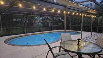 Un área de piscina al aire libre con un porche cubierto, asientos y luces colgantes.