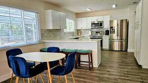 Una cocina moderna con armarios blancos, un refrigerador de acero inoxidable y una zona de comedor con sillas azules.