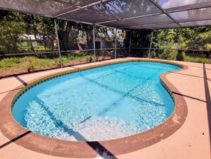 Une piscine à bord incurvé, entourée d’une zone abritée dotée d’une structure métallique et d’un toit.