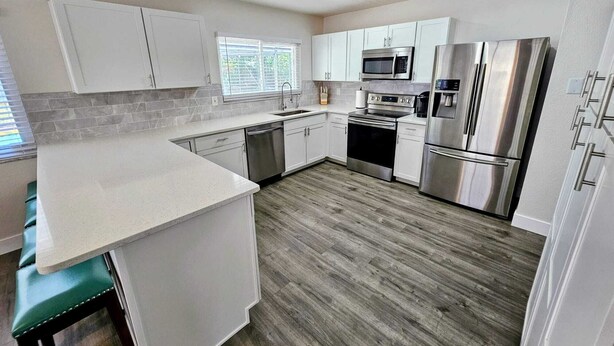 Una cocina moderna con armarios blancos, electrodomésticos de acero inoxidable y suelo de madera.