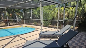 Un espacio exterior techado con piscina, sillones de descanso y una pérgola con luces colgantes.