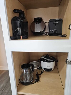 Une cuisine avec un aspirateur, un cuiseur à riz, un mijoteur et une machine à café, tous rangés sur les étagères.