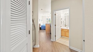 Ein Flur, der zu einem Schlafzimmer und Badezimmer mit Holzboden und weißen Wänden führt.