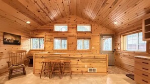 L’intérieur d’une cabane en rondins, avec un bar central en bois, de nombreuses fenêtres et un coin repas.