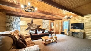 L’intérieur d’une cabane en rondins, avec un mur en pierre, un plafond en bois, un canapé en cuir, une table basse en bois et un téléviseur.