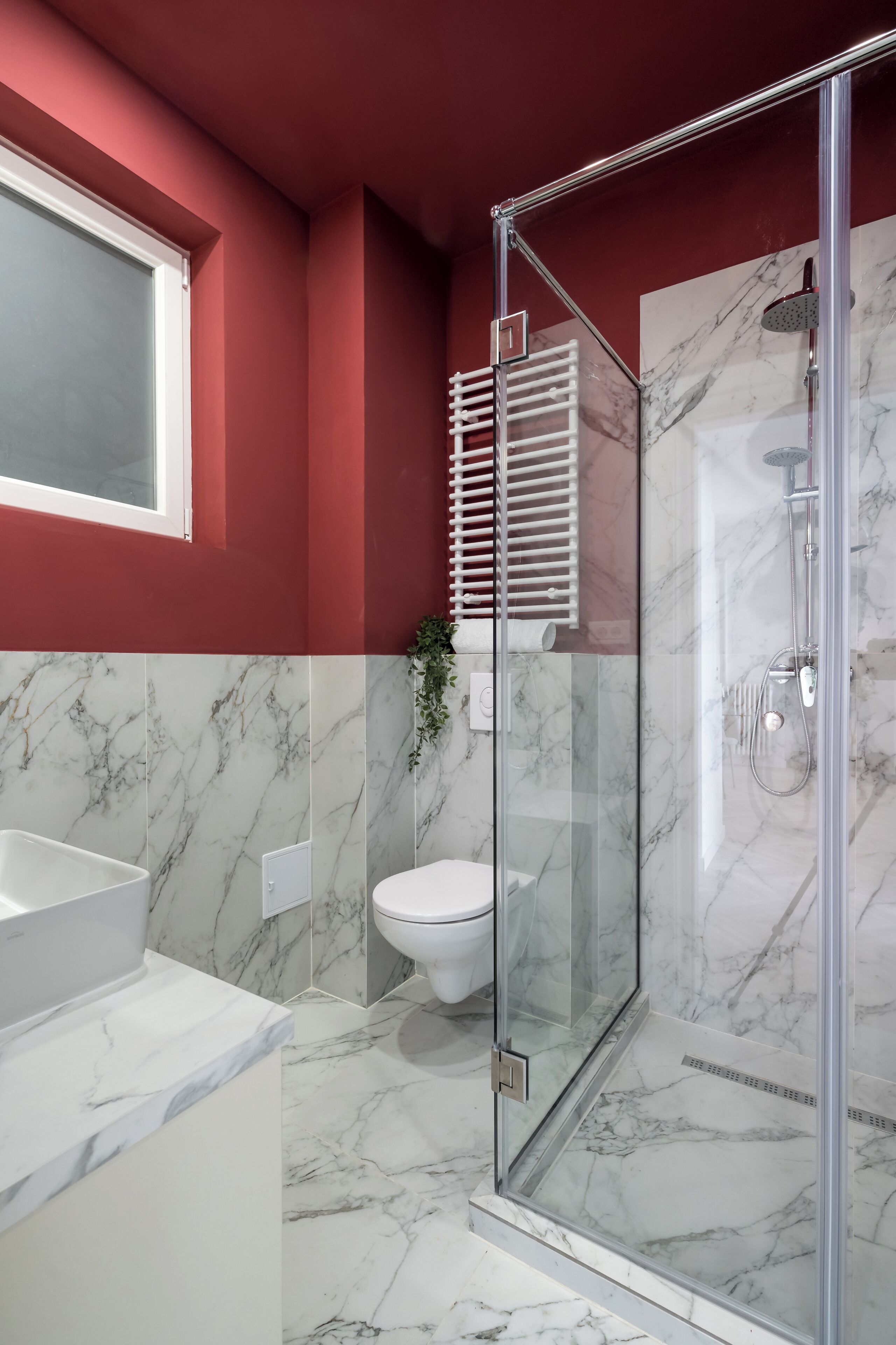 A modern bathroom with a glass shower enclosure, a white sink, and a marble-tiled floor.