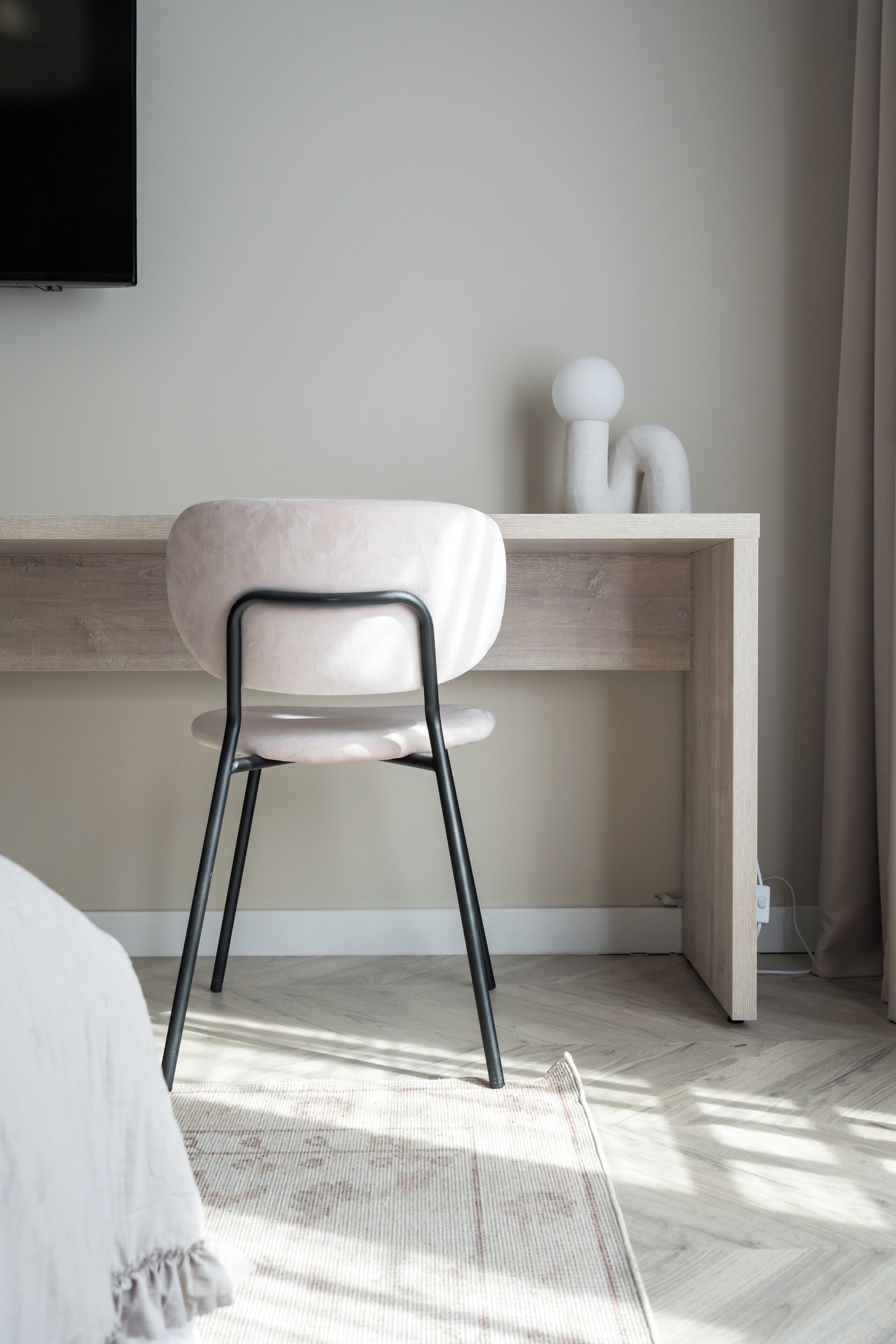 A modern bedroom with a wooden desk, a white chair, and a bed with a patterned bedspread.