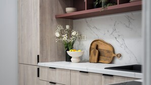 A kitchen with wooden cabinets, a marble backsplash, a white countertop, a wooden cutting board, a bowl of fruit, and a vase of flowers. - Refined & Spacious 3-Bedroom Flat Near Cismigiu, Balcony with Boulevard Views (Bucharest)