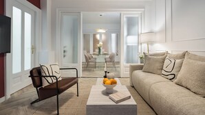A modern living room with a sofa, a coffee table with a bowl of fruit, and a television. - Refined & Spacious 3-Bedroom Flat Near Cismigiu, Balcony with Boulevard Views (Bucharest)