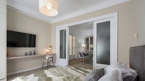 A modern hotel room with a bed, a desk, and a TV. - Refined & Spacious 3-Bedroom Flat Near Cismigiu, Balcony with Boulevard Views (Bucharest)
