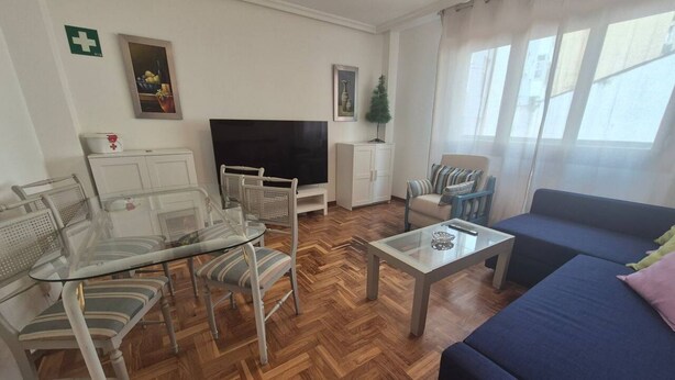 Een woonkamer met een bank, een televisie, een glazen tafel en een visgraatvloer.