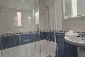 Een badkamer met een douchecabine van glas, een wit wastafelmeubel en blauwe betegelde wanden.