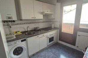 Une cuisine compacte équipée d’un lave-linge intégré, d’un évier et d’une fenêtre.
