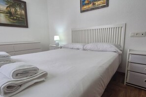 Un lit bien fait, avec du linge de lit blanc et des oreillers, une lampe de chevet et une table de chevet avec une lampe.