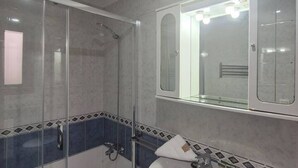 Une salle de bain dotée d’une douche à parois de verre, d’un grand miroir et d’un sol carrelé.