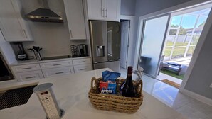 A modern kitchen with white cabinets, a stainless steel refrigerator, and a basket containing snacks and a bottle on the counter.