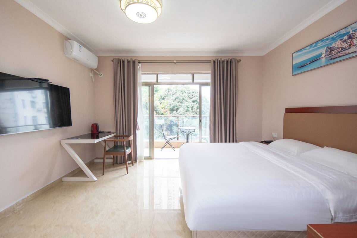 A hotel room with a bed, a desk, a chair, a TV, and a balcony with curtains.