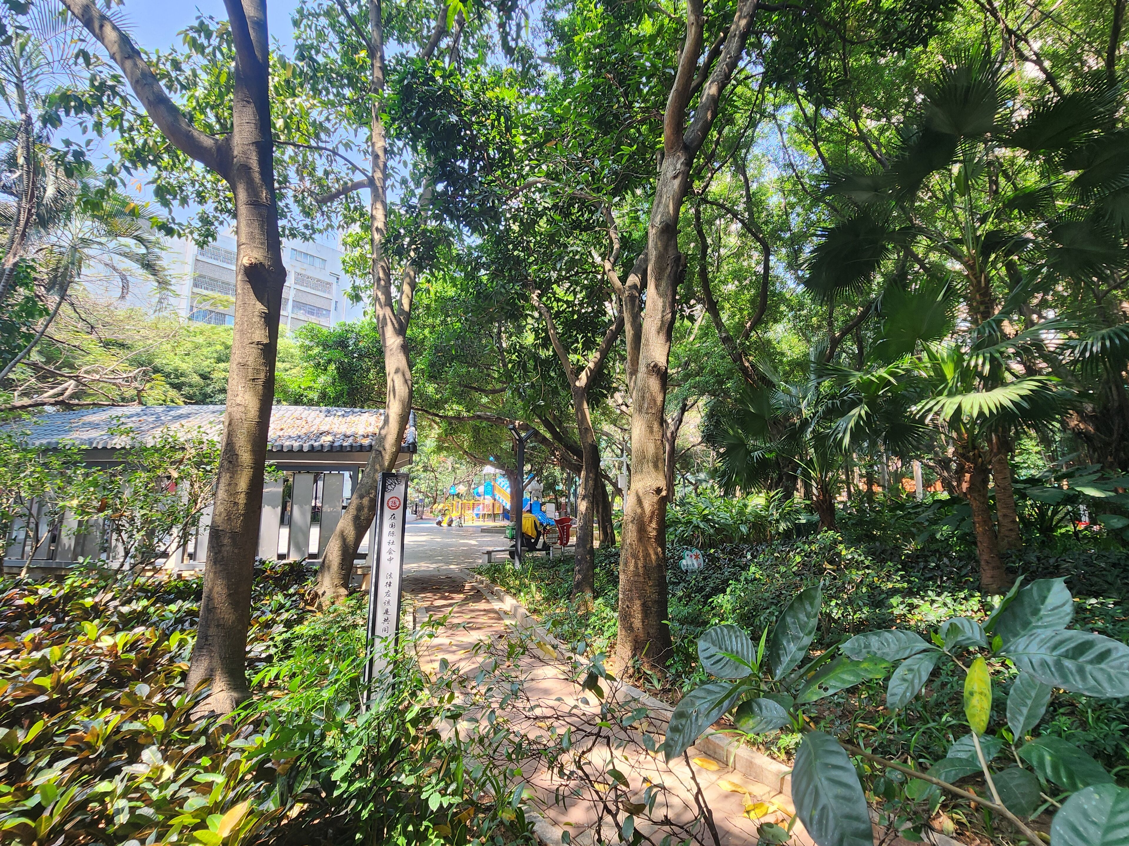 Un sendero atraviesa un jardín exuberante con árboles y plantas, que conduce a un edificio tradicional con tejado de azulejos.