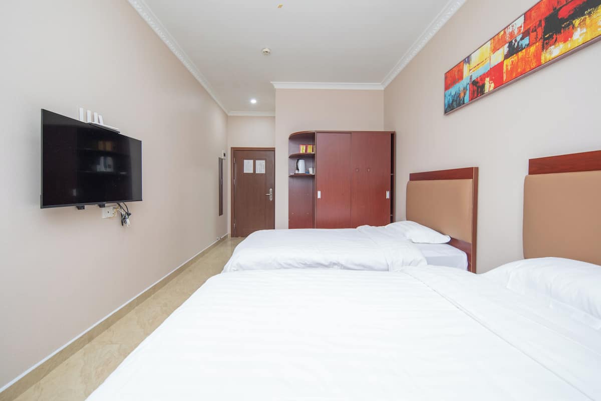 A hotel room with two beds, a TV mounted on the wall, a wardrobe, and a colorful painting on the wall.