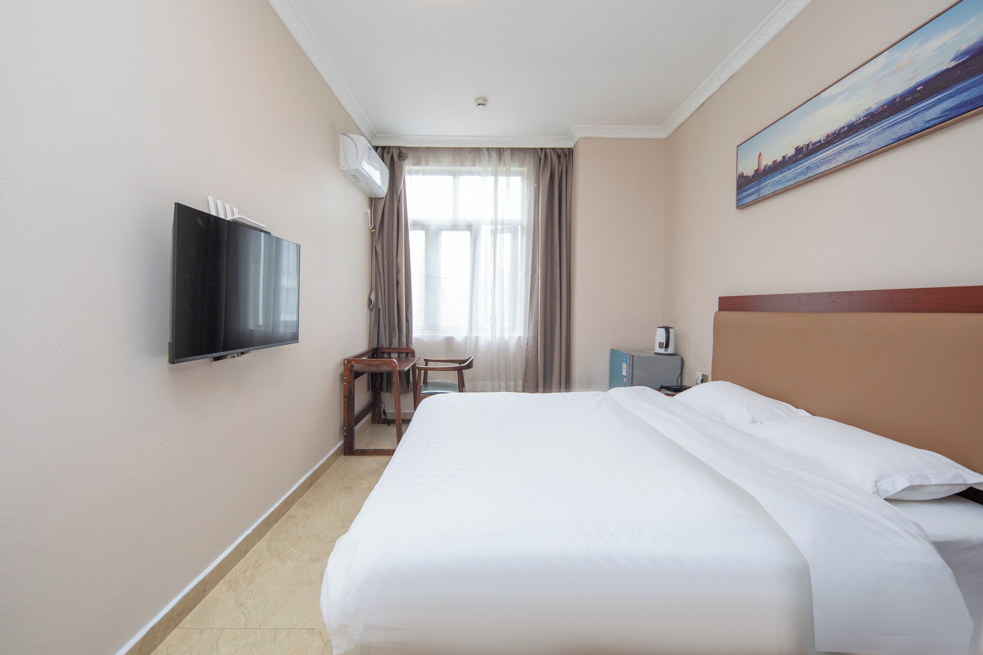 A hotel room with a bed, a TV, a desk, and a painting on the wall.