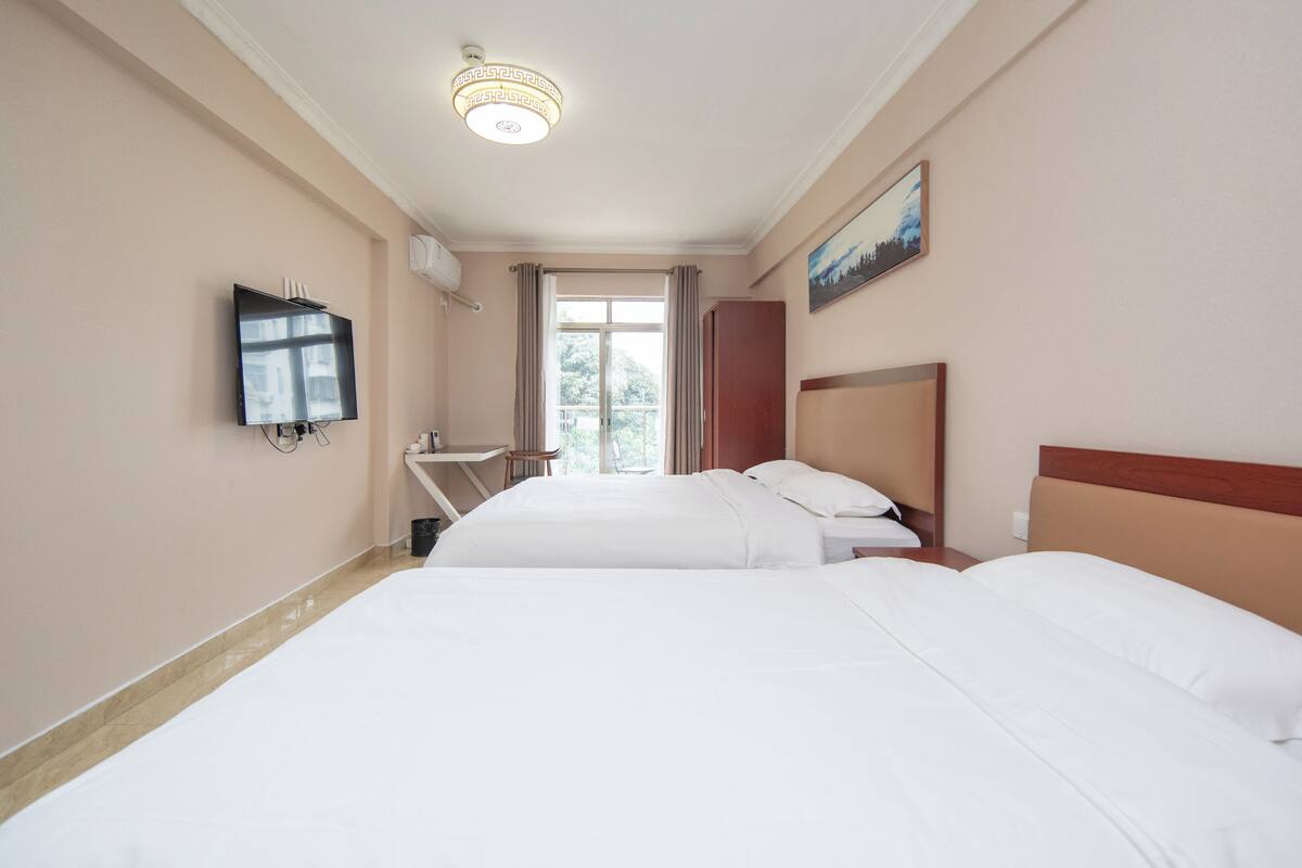 A hotel room with two beds, a television, a desk, and a window with curtains.
