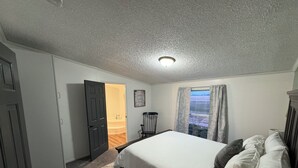 A bedroom with a bed, a door, a chair, a window with curtains, and a ceiling light. - Quiet. Relaxing. 4-bedroom House with AC, Jetted Tub and WiFi.  (Snover)
