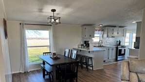 A spacious kitchen with a central island, wooden dining table, and bar stools. - Quiet. Relaxing. 4-bedroom House with AC, Jetted Tub and WiFi.  (Snover)
