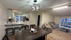 A modern kitchen with a marble countertop, a dining area with a dark wooden table and chairs, and a cozy living space with a sofa and a view of the outdoors. - Quiet. Relaxing. 4-bedroom House with AC, Jetted Tub and WiFi.  (Snover)