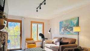 Un salon comprenant un canapé, un fauteuil, un banc, une lampe sur pied et un tableau accroché au mur.