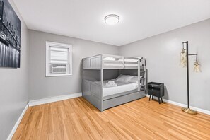 Ein Schlafzimmer mit Etagenbett, einem Fenster mit Jalousien, einer Stehlampe und einer Wand-Klimaanlage.