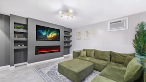 Una sala moderna con un sofá seccional, una chimenea y un televisor grande montado en la pared.