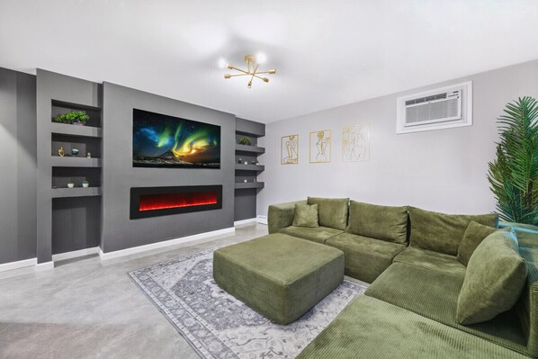 Ein modernes Wohnzimmer mit einer Eckcouch, einem Kamin und einem großen an der Wand befestigten Fernseher.