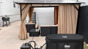 A covered outdoor seating area with a grill and speakers.