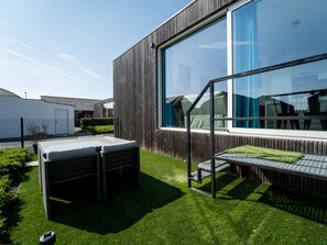 En moderne bygning med store vinduer, et overdækket udendørs siddeområde og en velplejet græsplæne.