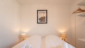 Ein Hotelzimmer mit zwei Betten, jedes mit einem gerollten Handtuch, Nachttischlampen und einem gerahmten Bild an der Wand.