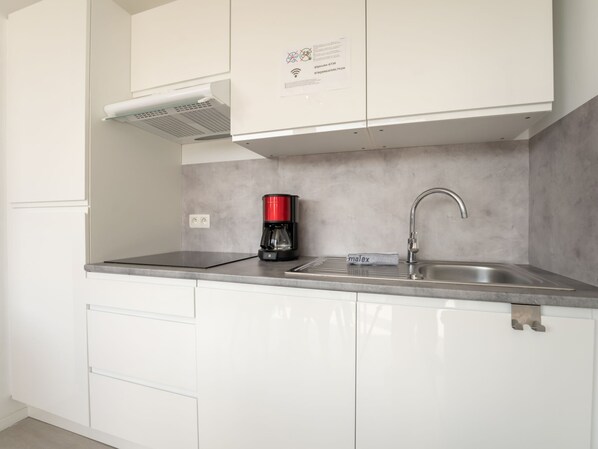 Una cocina moderna con armarios blancos, un lavamanos de acero inoxidable y una cafetera roja.