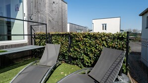 A modern outdoor seating area with two lounge chairs and a wooden fence.
