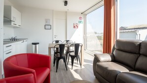A modern apartment with a dining area, a red chair, a brown sofa, and a large window with curtains.