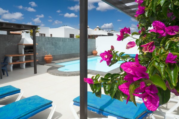 A poolside area with lounge chairs, a barbecue grill, and bougainvillea flowers.