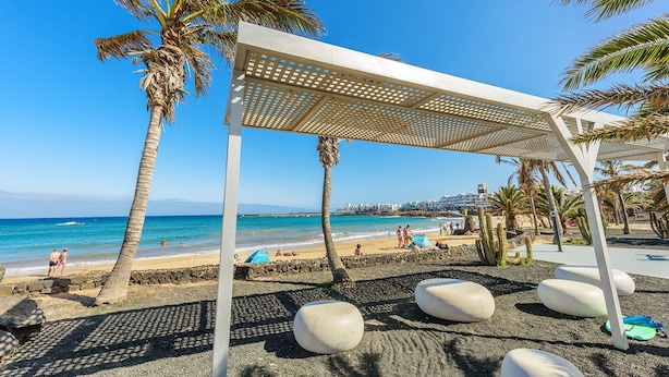 A beach with a white pergola, palm trees, and a clear blue sky. - Lanzahost "Casa Patricio" (Costa Teguise)