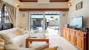 A modern living room with a sofa, coffee table, TV, and a sliding glass door leading to an outdoor patio with seating and a pool. - Lanzahost "Casa Patricio" (Costa Teguise)