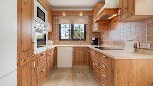 A kitchen with wooden cabinets, a dishwasher, a window with decorative iron bars, and a tiled backsplash. - Lanzahost "Casa Patricio" (Costa Teguise)