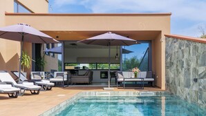A modern outdoor pool area with lounge chairs and umbrellas, a dining area with a table and chairs, and a stone wall. - Villa Ana by Interhome (Novigrad (Istra))