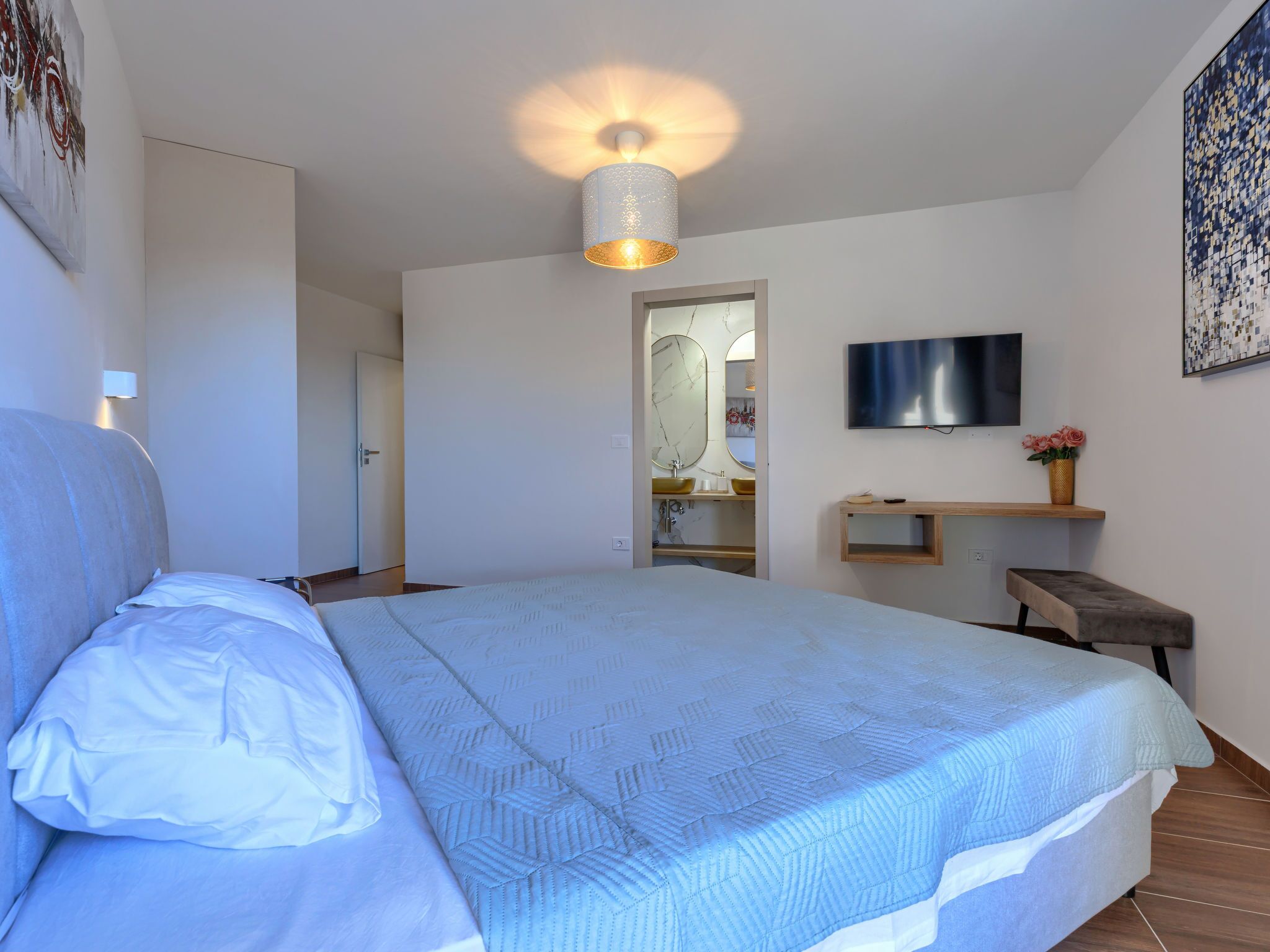 A bedroom with a bed, a TV, a mirror, and a bathroom visible through an open door.